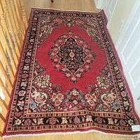 Photo of the full red Persian rug showing central floral medallion and border design on hardwood floor.