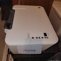 Angle view of white HP DeskJet 3520 printer showing the control panel and output tray, with a note of size 17 x 12 x 6 inches taped to the front.