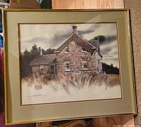 Framed signed print of a stone house with matting and gold frame, view of entire artwork and frame.