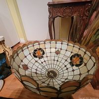 Top-down angled view of the full stained glass lampshade, showing circular, geometric, and floral pattern in beige, white, red, orange and black glass.