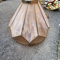 Close-up view of the base and bottom edge of the Tiffany style lamp showing brass colored metal base and the bottom parts of the pinkish-beige swirled glass shade panels with brass framing.