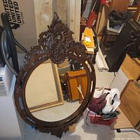 Full view of walnut wood framed ornate decorative mirror with oval glass and extensive carved floral and scroll wood details.