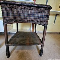 Front angle view of the dark brown wicker side table showing the woven wicker construction and lower wicker shelf.