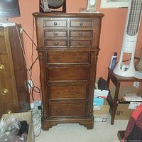 Front view of tall wooden jewelry cabinet showing six small upper drawers and four larger lower drawers with dark wood finish and round knobs, turned columns on sides, sitting on carpet.