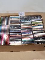 Top view of a full box of neatly stacked compact discs showing varied artist names and album titles on spines