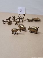 Top view of collection of 11 brass animal figurines including horse, goat, swan, pig, rhinoceros, dog on rock, crocodile, and animal-shaped scoop