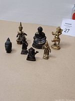Seven vintage Asian religious brass figurines displayed together with a soda can for scale. Varied patina and brass finishes.