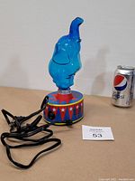 Blue glass elephant lamp unlit next to a Pepsi can for scale