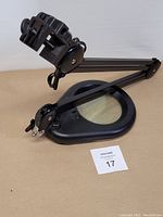 Magnifying lamp laid flat showing adjustable arm and clamp base with magnifying glass.