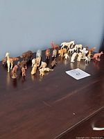 Full view of 24 assorted miniature animal figurines arranged on table against a blue wall.