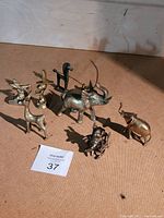 Group of eight miniature brass animal figurines arranged on a brown surface showing size and detail.