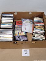 Photo of box with stacked music CDs seen from above, showing a large quantity of mixed popular music CDs.