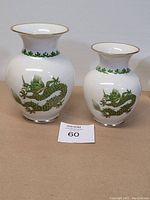 Two white porcelain vases featuring green dragon design and gold accents, with a paper tag labeled 60 in front of them