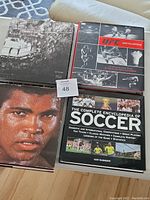 Top view of three oversized sports books including UFC encyclopedia, soccer encyclopedia, and Octagon by Kevin Lynch UFC photo book.