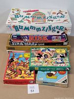 Photo of vintage board games stacked showing titles Hummzinger, Star Wars Risk, Clue, The Game of Adventure along with two Disney puzzles.