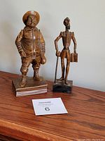 Photo showing two hand carved wooden Spanish statues, one stout man and one slender man, standing on wooden bases