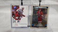 Two Eric Staal rookie hockey cards displayed upright in protective sleeves. One card shows Staal in white uniform with holographic SPx logo.