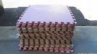 Stack of square foam interlocking floor mats in alternating pink and beige colors showing edges and surface texture.