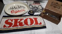 Photo showing Carlsberg beer tray, Skol towel, war magazine, round tin, and La Selecta box with darts.