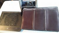 Photo showing brown leather briefcase front above black laptop stand fan with ventilation grill and black binoculars placed behind.