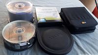 Overview of lot including multiple DVD-R spindles, DVD/CD sleeves box, black oval hard case and black CD/DVD storage binder