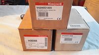 Photo of three Honeywell solenoid valve boxes stacked showing the model number V4295S1005 and voltage rating 110/120V on labels.