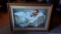 Front view of large framed print showing reclining woman and detailed folds of fabric. Frame shows wear and damage.