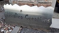 Metal sign with cutout text 'Metalica Creations' on an irregular mountain-top shaped metal sheet.