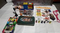Photo showing assorted Three Stooges items including plush doll, grey elephant, collectible tin, small toy figures, collectible magazines, and Rubik's cube puzzle toy.