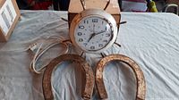 Photo showing two heavy metal horseshoe trivets and a vintage electric clock with wooden frame lying on a gray cloth surface.