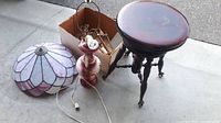 Photo showing a small wooden table, a ceramic lamp with cord, and a stained glass lamp shade on the floor
