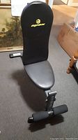Workout bench in upright backrest position with visible Apex logo and foam rollers at footrest.