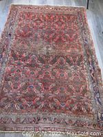 Full view of rug laid flat showing red field with intricate floral and geometric pattern and beige border.