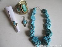 Four jewelry pieces laid out together: necklace, cuff bracelet, pendant, ring on white surface