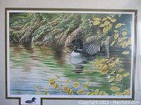 Full view of lithograph artwork behind glass showing a loon on water with foliage and yellow leaves.