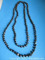 Full view of the extra long strand of dark natural Tahitian pearls laid out against a blue background.
