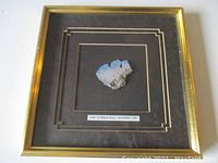 Frontal view of the concrete piece of Berlin Wall mounted in a gold wooden shadowbox frame with black matte and gold inner lines.