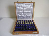 Open wooden carry case showing hand carved white and black marble chess pieces arranged inside a blue velvet interior with satin-lined lid.