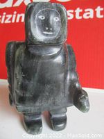 Front view of a carved black stone Inuit man figurine with simple facial features drawn on. Standing position with rounded arms and legs.