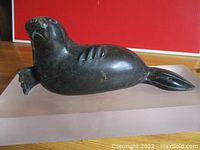 Side view of dark stone walrus carving mounted on pink acrylic base against red background, showing full length and shape