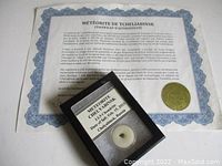 Photo showing the meteorite fragment inside a clear display case with the certificate behind it.