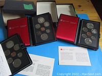 Three RCM coin sets in black leather-like presentation folders with red interior, containing multiple coins each including silver double dollar coins