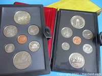 Two opened black leather-like folders displaying Canadian silver dollar coin sets with multiple coins of varying denominations and sizes arranged in molded cases.