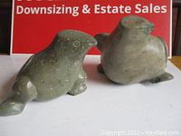 Two large stone bird carvings placed side by side on a white surface with red signage background