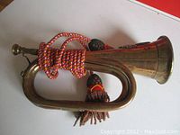 Full side view of the Royal Welsh Fusiliers battle bugle featuring copper and brass construction with decorative cord and tassels wrapped around the tubing.