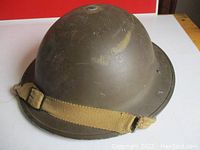 Front and side view of olive green metal military helmet with fabric chin strap.