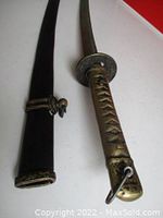 Sword partially withdrawn from scabbard showing handle grip details and scabbard tip.
