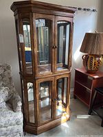 Front view of oak-finish curio cabinet showing dual glass doors, crown molding, and base
