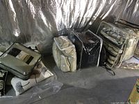Several packaged bedding sets and cushions arranged on a basement floor with reflective insulation behind.