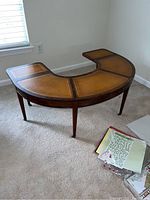 Front angle view of the vintage U-shaped wooden coffee table showing drop leaf ends and leather top inset.